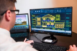 Architect reviewing detailed 3D building models on dual monitors in a modern office, illustrating equipment financing success for an architectural consulting firm