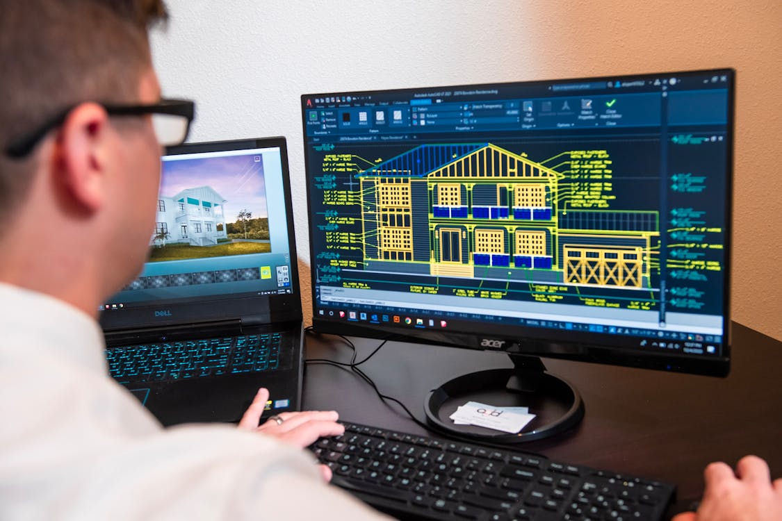 Architect reviewing detailed 3D building models on dual monitors in a modern office, illustrating equipment financing success for an architectural consulting firm