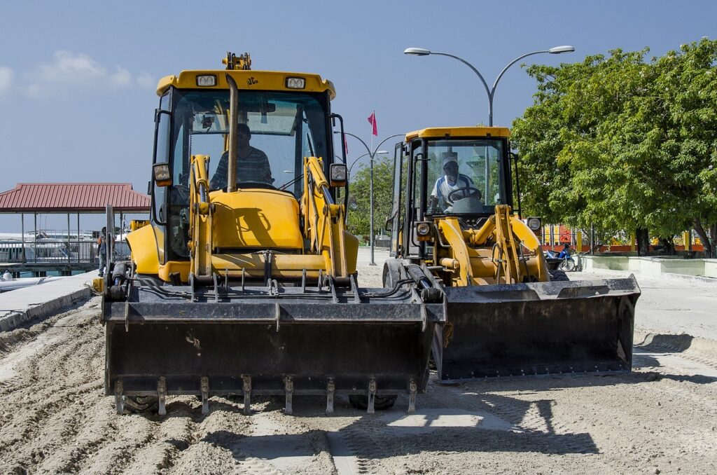Workers and heavy machinery paving a road under a clear sky, with asphalt rollers and construction crew actively spreading and compacting the surface