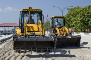 Workers and heavy machinery paving a road under a clear sky, with asphalt rollers and construction crew actively spreading and compacting the surface